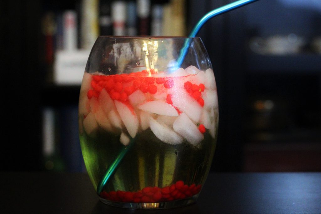 A large punchbowl drink with a green liquid, ice cubes, and red candies.