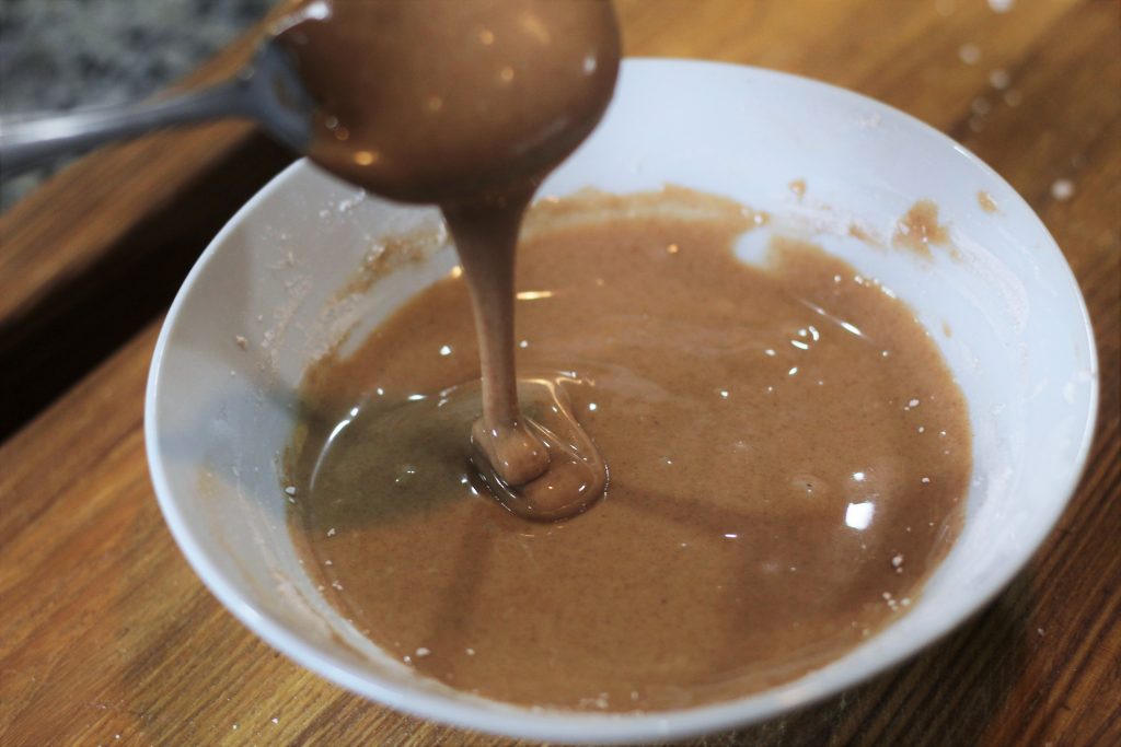 The mixed glaze with a spoon drizzling some back into the bowl.