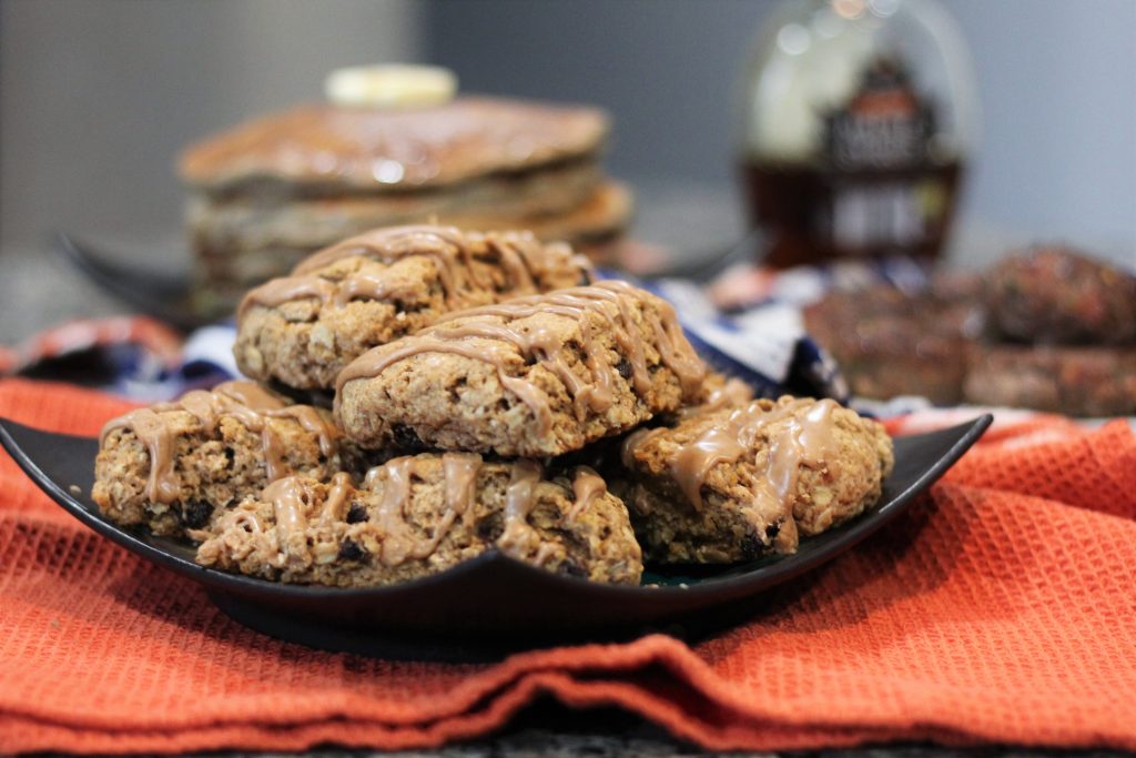 The scones piled on a plate. Pancakes, maple syrup, and sausages are out of focus in the background. 