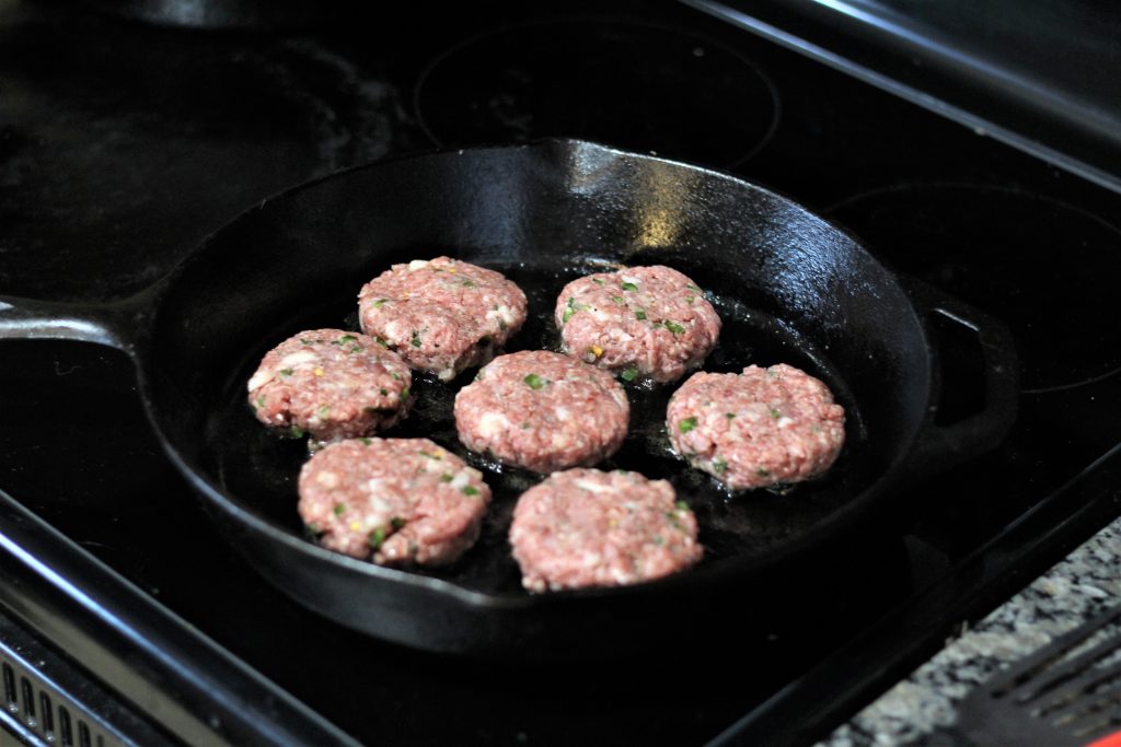 7 patties in a cast iron skillet being cooked.