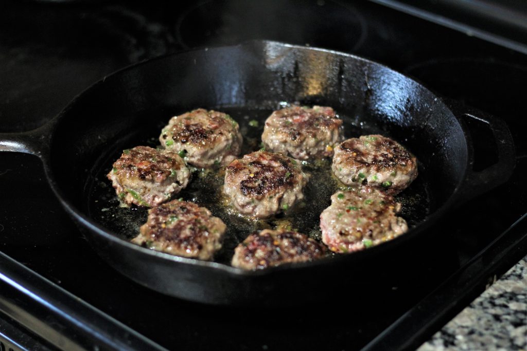 8 patties in a cast iron skillet being cooked.