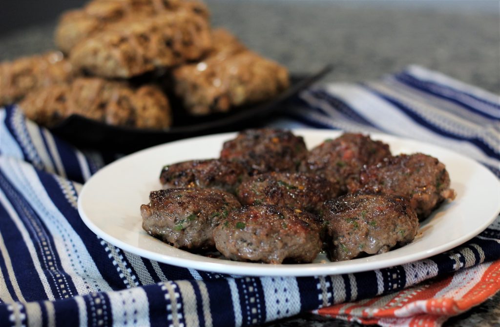 Patty sausages on a plate. Scones can be seen in the background.