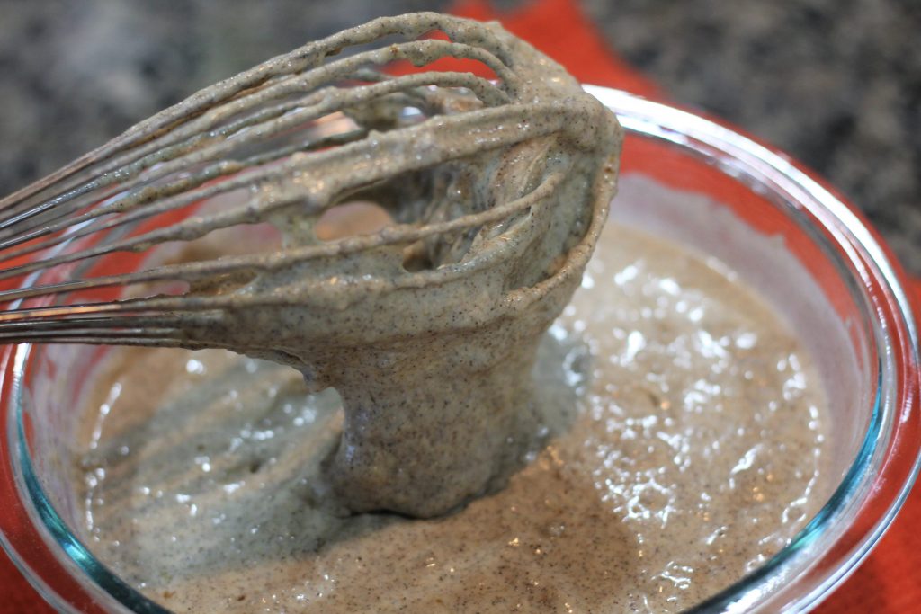 Whisk held above the bowl of batter to show the batter dripping into the bowl. 