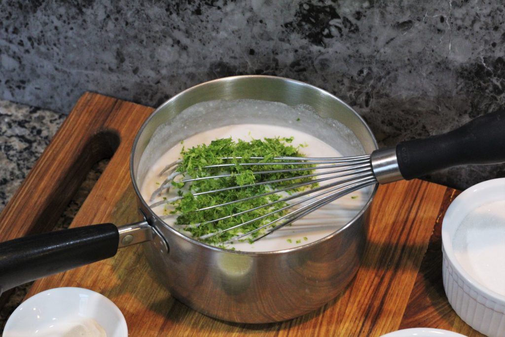 A saucepan with coconut milk and cream and lime zest being whisked together. 