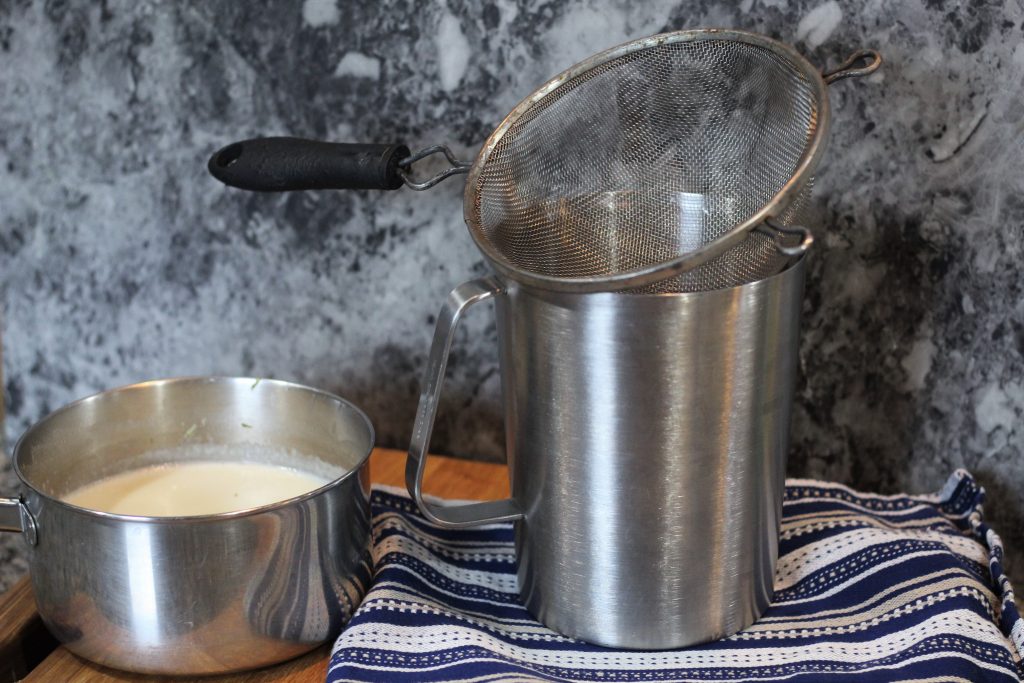 A fine wire strainer atop a metal pitcher. 