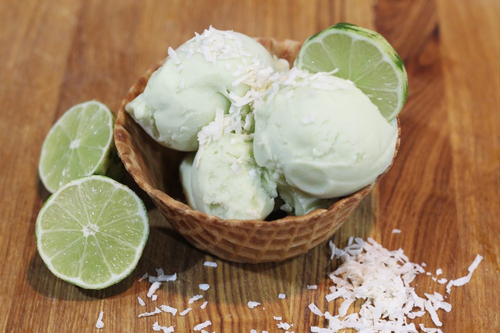 Waffle cone bowl with scoops of lime ice cream topped with coconut flakes and a lime slice.