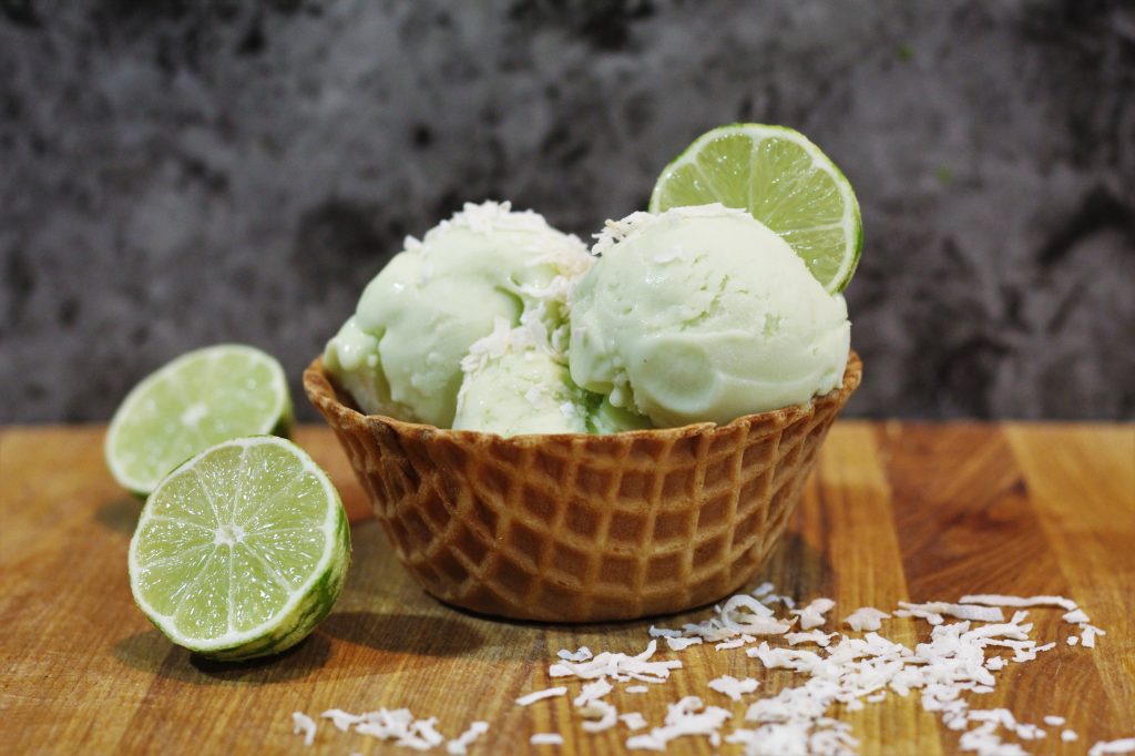 Waffle cone bowl with scoops of lime ice cream topped with coconut flakes and a lime slice.