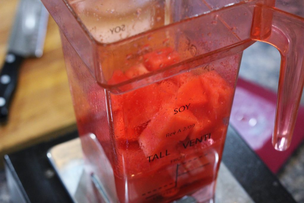 A clear pink blender canister filled with watermelon and other ingredients. 