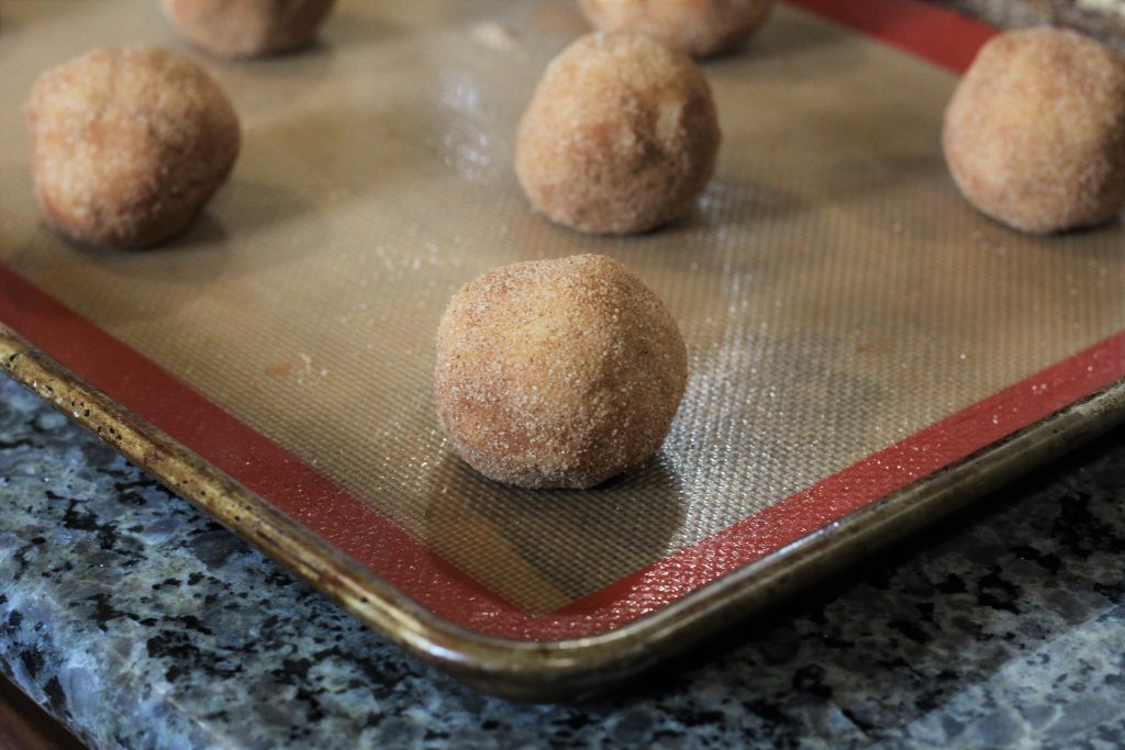 Balls of dough coated in sugar mix on a baking sheet.