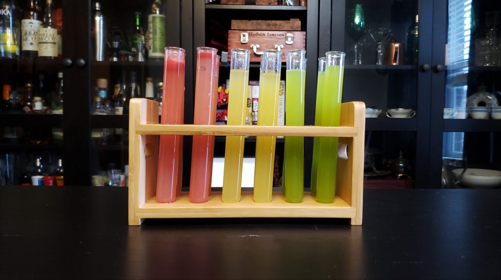 A rack of test tubes in 2 rows of 6. The first 2 by 2 section are pink, the next section are yellow, and the final section are green.