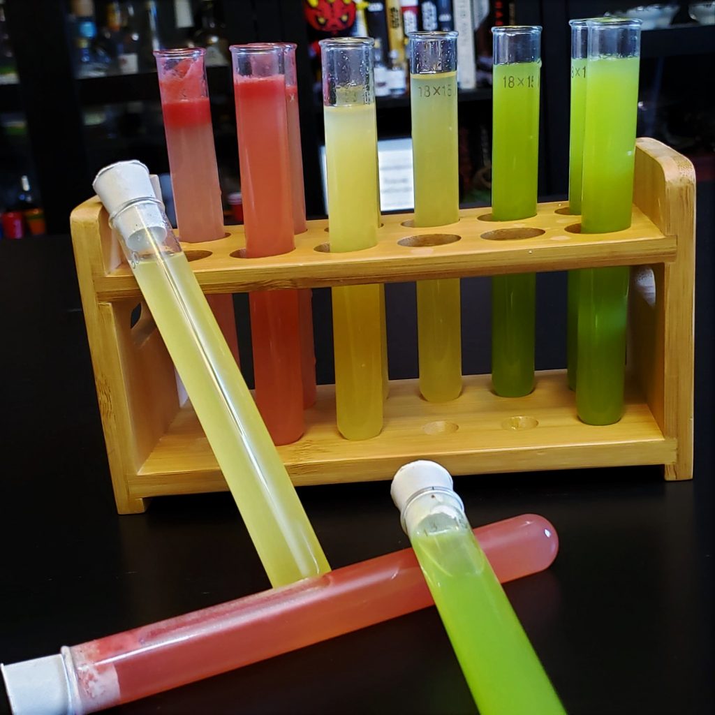 A rack of test tubes in 2 rows of 6. The first 2 by 2 section are pink, the next section are yellow, and the final section are green.
1 yellow, 1 pink, and 1 green tube have been taken out and arrange on the table in front of the rack. 