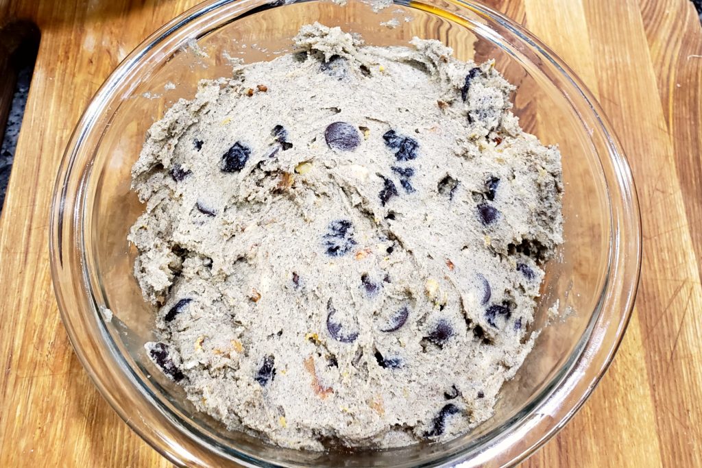 A glass bowl of the dough, showing the chunks of fruits, chocolate, and nuts, 